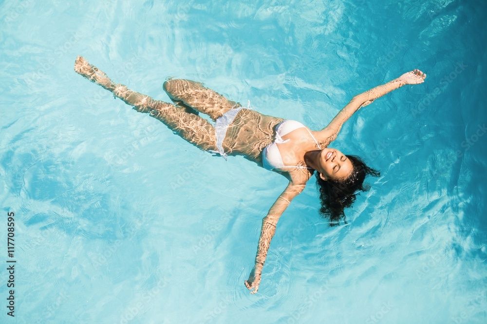 Young woman in a swimsuit floating in a large resort swimming pool